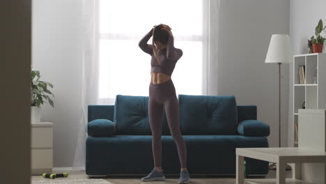 young-sexy-woman-is-warming-body-before-training-at-home-moving-head-to-sides-standing-in-living-room-sport-activity-and-healthy-lifestyle